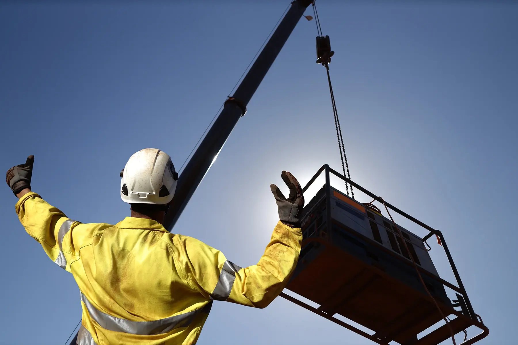 Rigger wearing a glove standing raising using his hands signal by moving finger slowly to directing communication with crane driver to move the boom up at construction site
